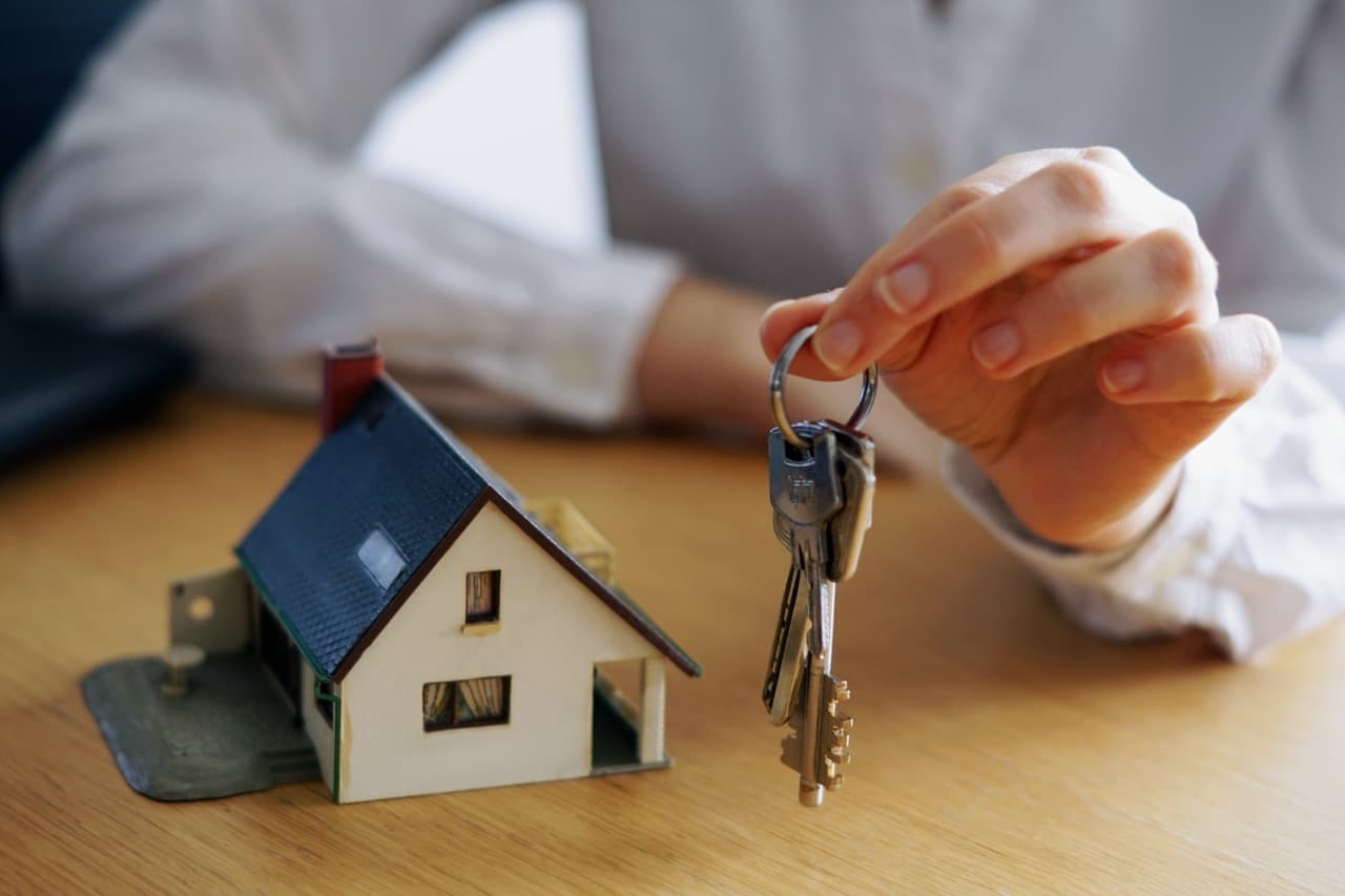Hand holding keys next to a model house